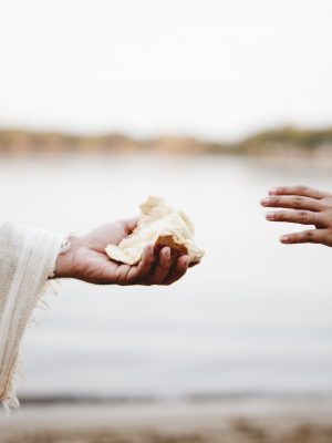 A closeup shot of a person wearing a biblical robe giving bread to another person with a blurred background